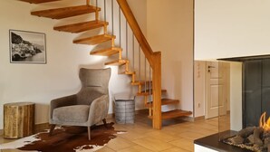 Ein modernes Wohnzimmer mit einer Wendeltreppe aus Holz, einem grauen Sessel, einem Kuhfellteppich, einem Kamin und einem gerahmten Bild an der Wand.