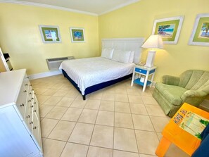 Ein Schlafzimmer mit einem Bett, einem Nachttisch, einem Sessel, einer Kommode und einer Wand mit gerahmten Bildern.