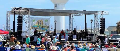 A stage with a crowd of people, a water tower, and a beach music festival banner.