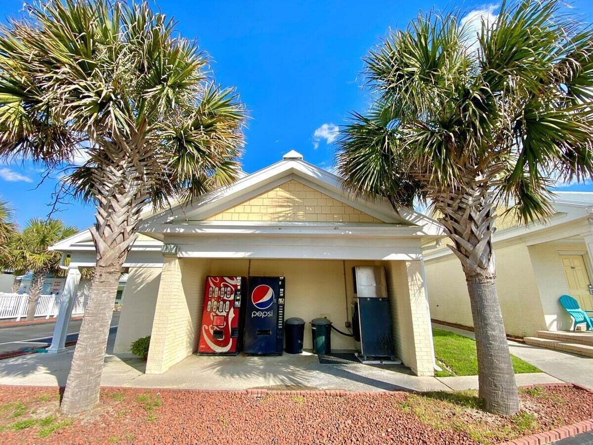 A building with a small entrance, palm trees, a Pepsi vending machine, and a Coca-Cola vending machine.