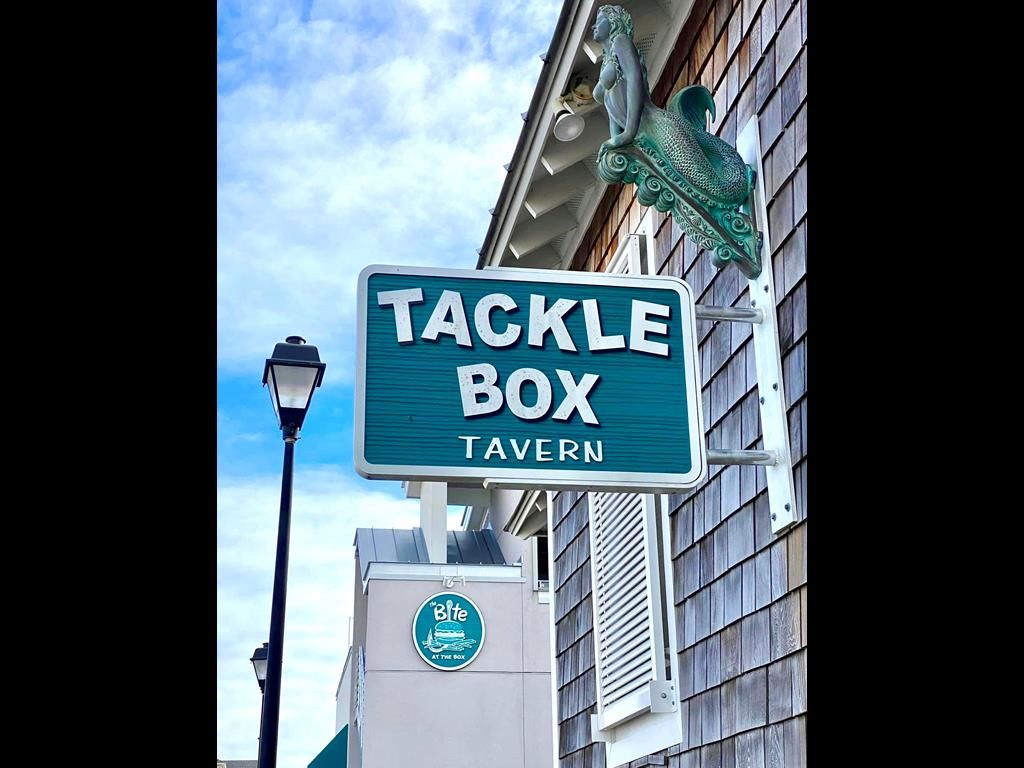 Un letrero para 'Tackle Box Tavern' con un logotipo debajo.