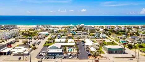 An aerial view of a coastal town with residential buildings, a main road, and a beach in the background.