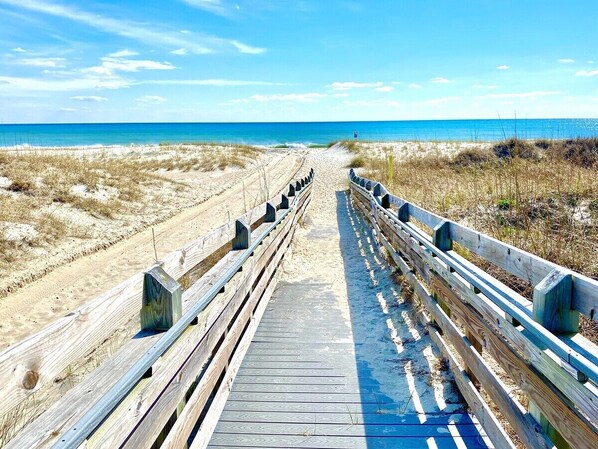 A wooden boardwalk leading to the beach with a clear sky.