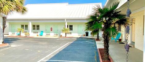 A motel with a parking lot, a building with a white roof, and a palm tree.