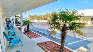 A covered outdoor seating area with blue chairs, a palm tree, and a parking lot in the background. - Pet-friendly, 3 Blocks to Beach, Pool, #305 (Atlantic Beach)