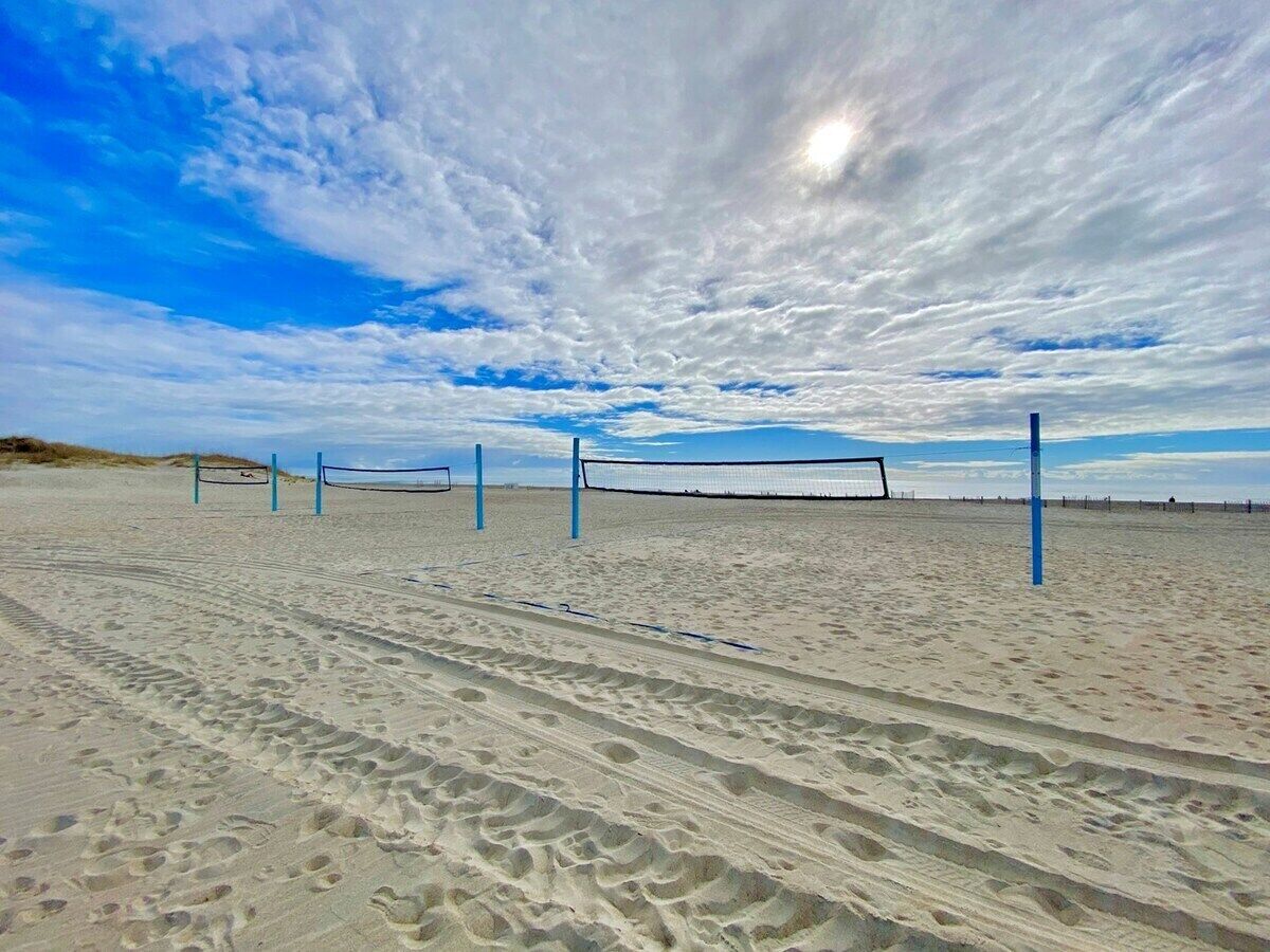 Una spiaggia con un campo da pallavolo sulla sabbia, delimitato da reti e pali blu.