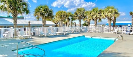 A swimming pool with a white fence, palm trees, and a clear blue sky.