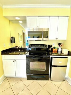 A kitchen with white cabinets, a black stove, a microwave, and a refrigerator. - Pet-friendly, 3 Blocks to Beach, Pool, #402 (Atlantic Beach)
