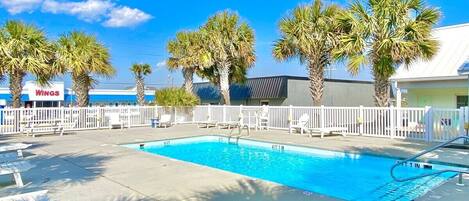 A swimming pool with a white fence, palm trees, and a building with a sign that reads 'WINGS' in the background.