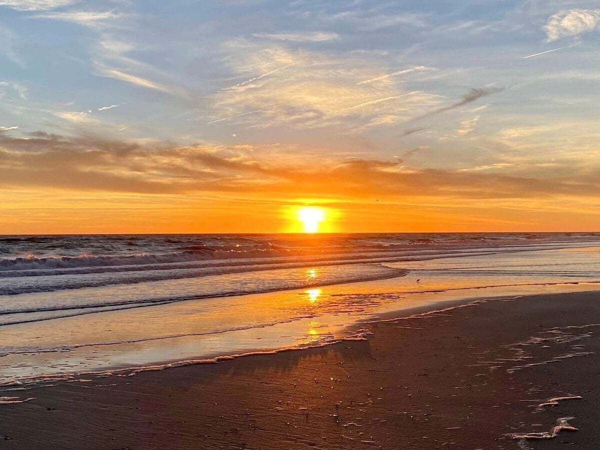 Escena de playa con atardecer, olas y cielo despejado.