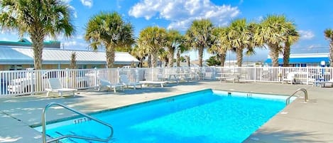 A swimming pool with a white fence, palm trees, and a clear blue sky.