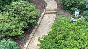 A paved garden pathway surrounded by lush greenery and a decorative fountain. - 2 BR Hidden Gem with Lake Access, Pool & Hot Tub 15 Min from Lanier Islands  (FLOWERY BRANCH)