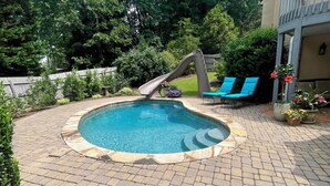 A backyard with a swimming pool, a slide, and two blue lounge chairs. - 2 BR Hidden Gem with Lake Access, Pool & Hot Tub 15 Min from Lanier Islands  (FLOWERY BRANCH)