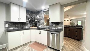 A modern kitchen with white cabinets, a black countertop, and a stainless steel dishwasher. - 2 BR Hidden Gem with Lake Access, Pool & Hot Tub 15 Min from Lanier Islands  (FLOWERY BRANCH)