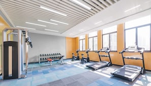 Un gimnasio con equipo de ejercicio, incluyendo cintas de correr y mancuernas, y ventanas amplias que dejan entrar luz natural.