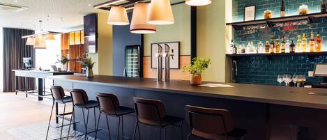 A modern bar area with a long counter, bar stools, and a variety of bottles and glasses on shelves.