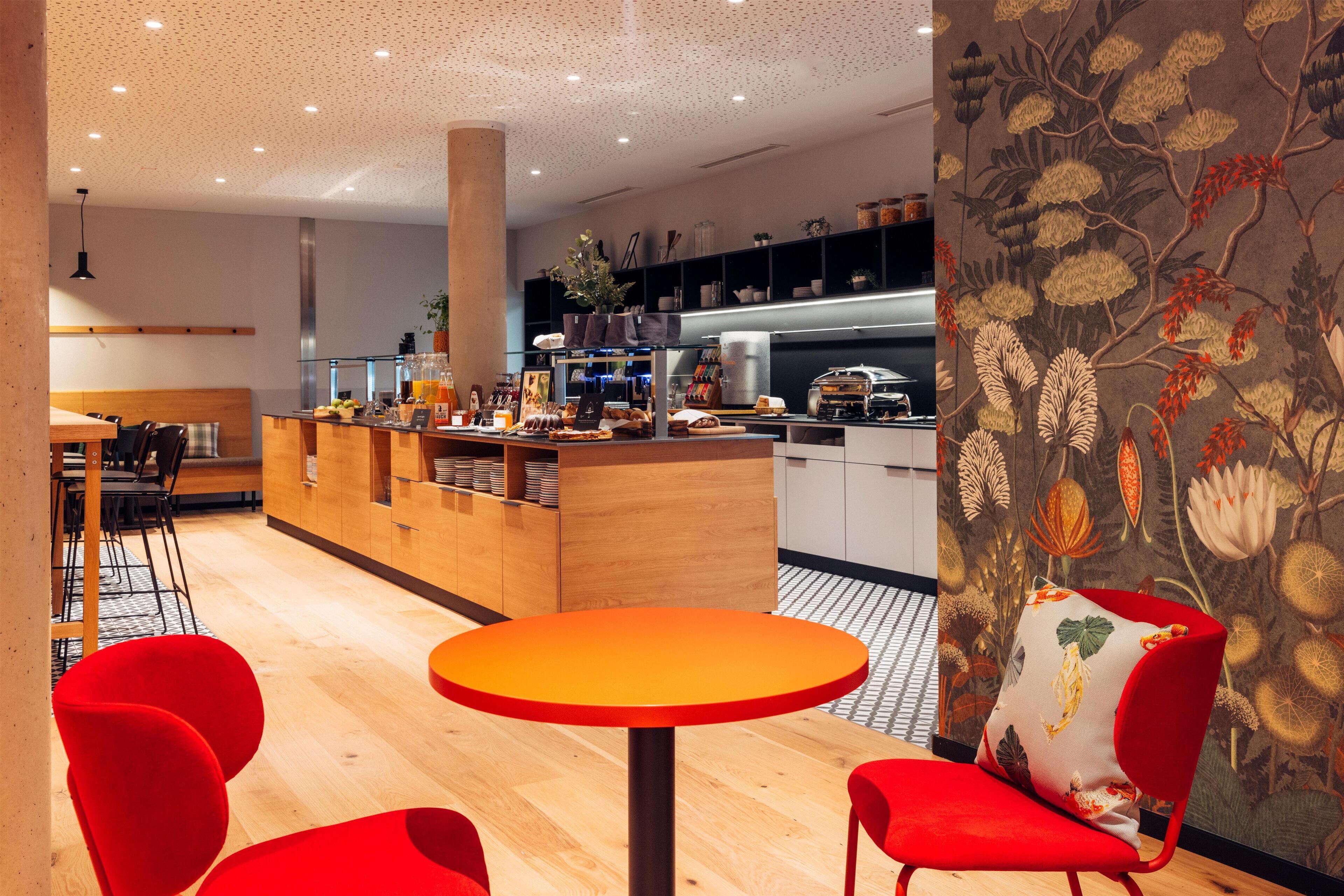 Ein modernes Interieur mit einer zentralen Holztresen, roten Stühlen und einer Wand mit Muster.