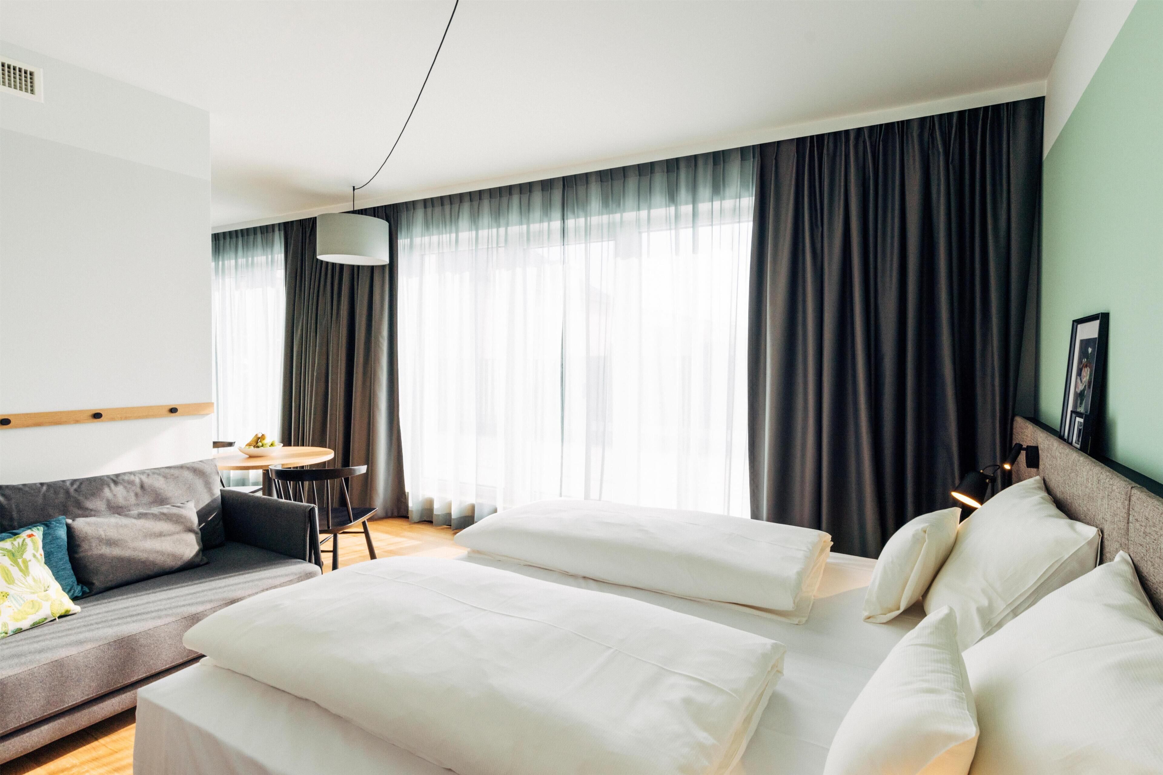 A hotel room with a bed, a sofa, a dining table, and a chair.