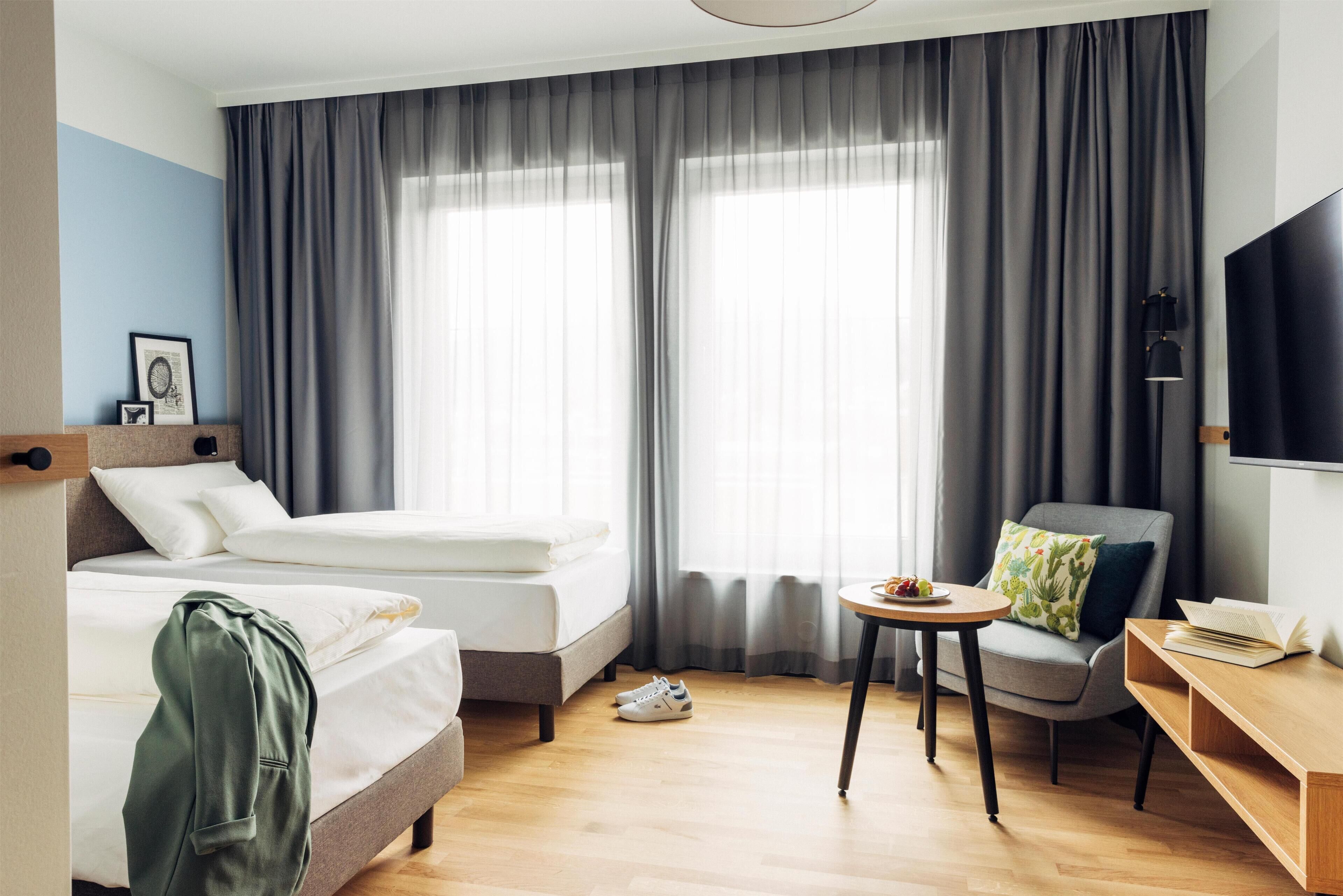 A hotel room with a bed, a chair, a small table, and a TV.