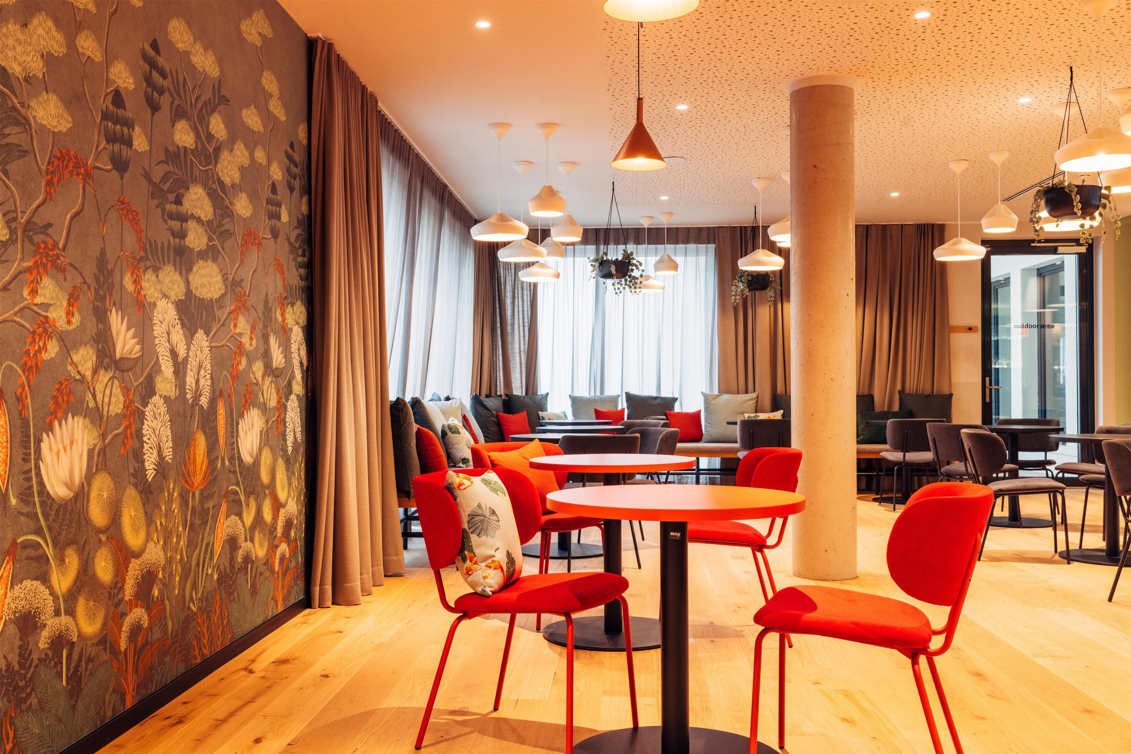 A modern interior with wooden flooring, red chairs, and tables arranged in a cozy dining area.