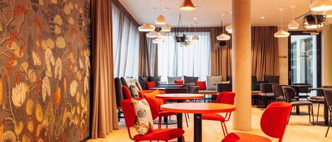 Un interior moderno con suelo de madera, sillas rojas y mesas dispuestas en una zona de comedor acogedora.