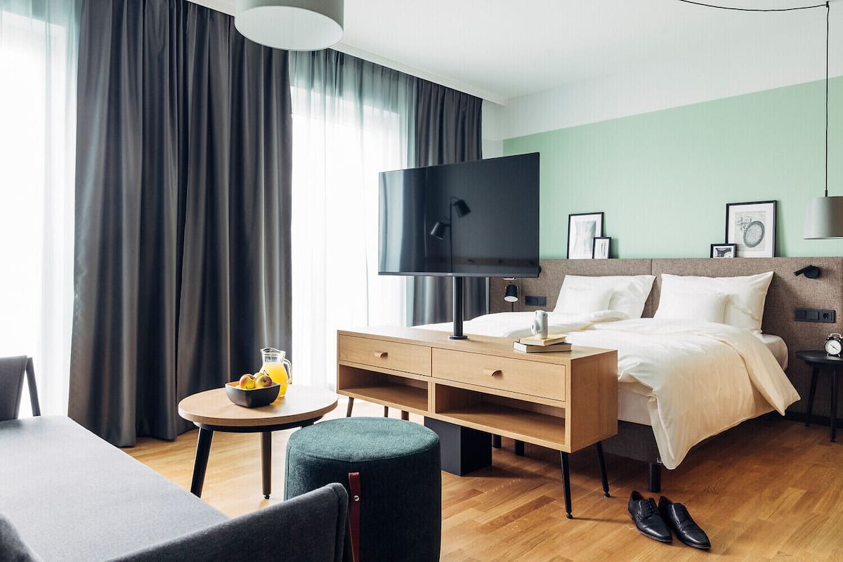 Habitación de hotel con cama, escritorio, silla, televisor y una mesita con fruta y bebida.