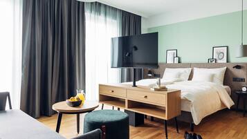 Ein Hotelzimmer mit einem Bett, einem Schreibtisch, einem Sessel, einem Fernseher und einem kleinen Tisch mit Obst und Getränken.