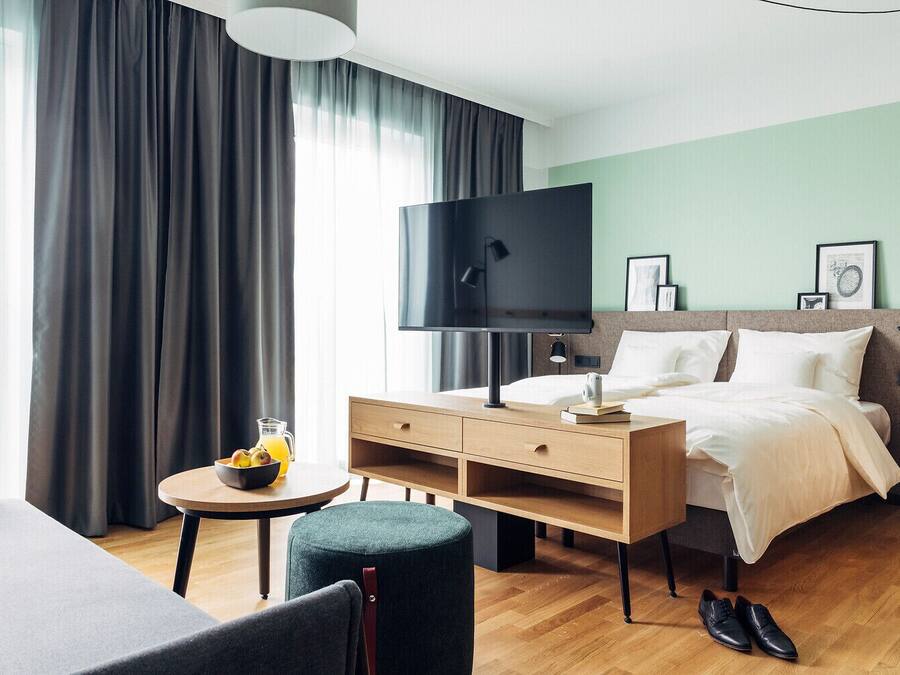 Ein Hotelzimmer mit einem Bett, einem Schreibtisch, einem Sessel, einem Fernseher und einem kleinen Tisch mit Obst und Getränken.