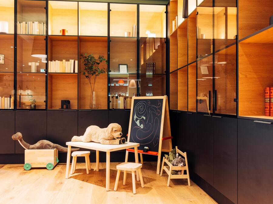 A cozy reading nook with a wooden table, chairs, a chalkboard, and a bookshelf filled with books and decorative items.