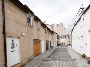 A narrow cobblestone street lined with traditional buildings, featuring a mix of wooden and metal doors, and a variety of architectural styles.