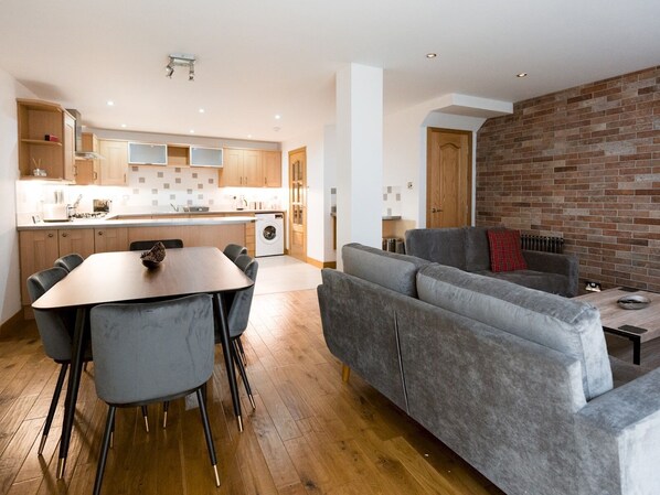 A modern living room with a grey sofa and a dining table with chairs.