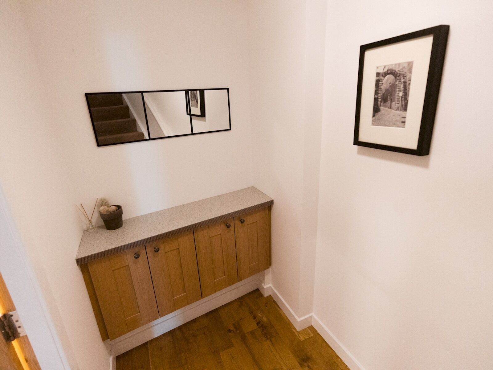 Un couloir avec une armoire en bois, un miroir et un tableau encadré accroché au mur.
