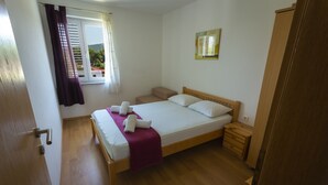 A bedroom with a wooden bed, a nightstand, a wooden wardrobe, a window with curtains, and a wall-mounted mirror.