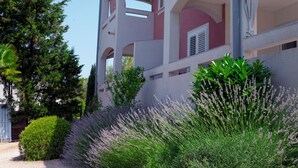 A multi-story building with balconies, surrounded by lush greenery and lavender plants.
