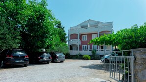 A two-story building with a red and white facade, parked cars in front, and a gravel driveway.