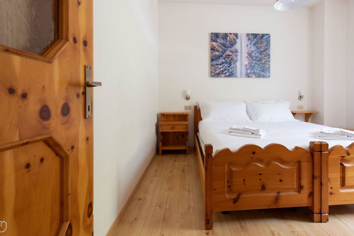 A wooden-framed bed with white bedding, a nightstand, and a wall-mounted painting.