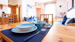 A dining table set with plates, glasses, and cutlery, surrounded by wooden chairs and a blue placemat. - Italianway - Belvedere 28 (Valdidentro)