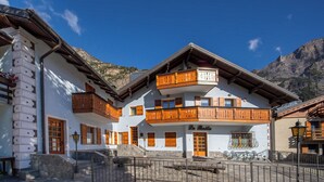 A traditional Alpine-style building with wooden balconies, stone steps, and a mountain backdrop. - Italianway - Belvedere 28 (Valdidentro)