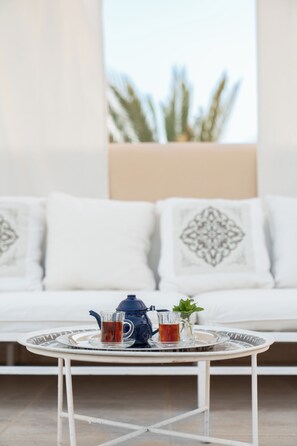 A round white table with a blue teapot and two glasses of tea, set on a balcony with a white sofa and patterned cushions in the background. - JAZ Neo Almazino, Almaza Bay (Marsa Matrouh)