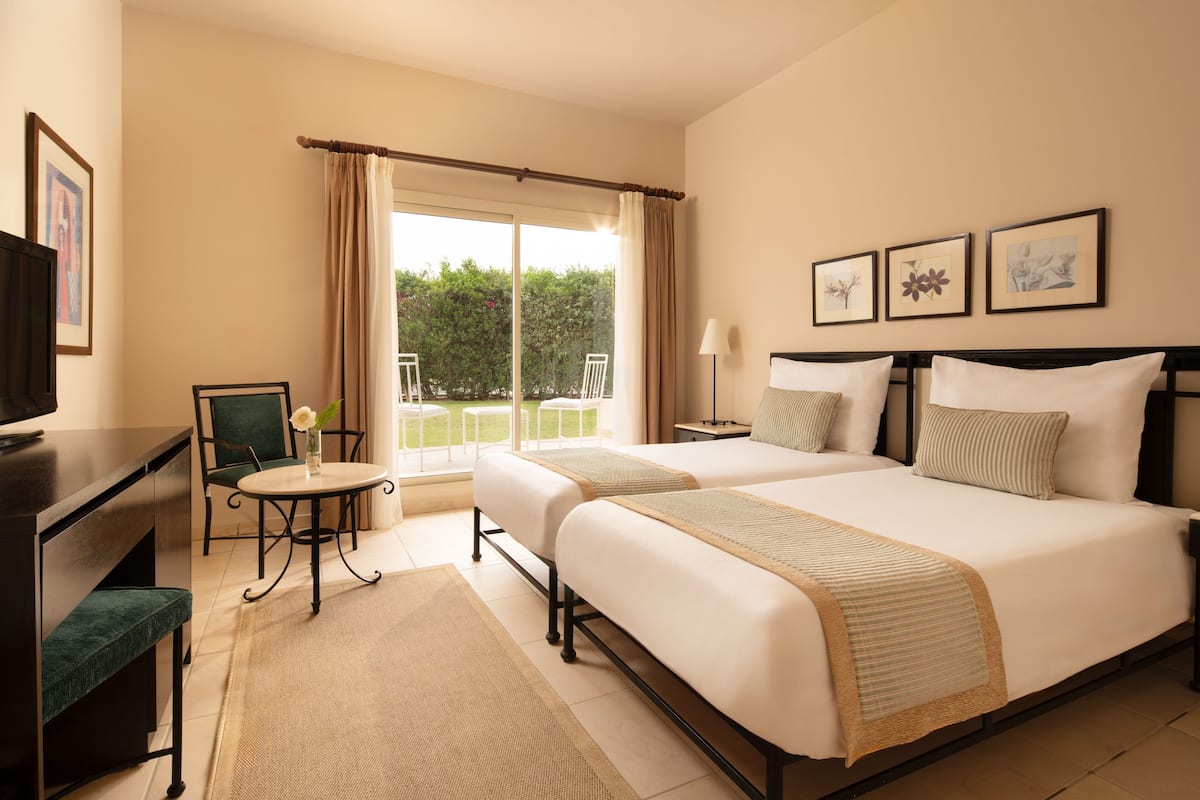 Ein Hotelzimmer mit zwei Betten, einem Schreibtisch, einem Stuhl, einem kleinen Tisch und Blick ins Freie.