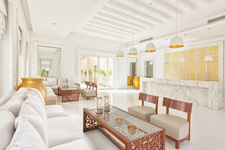 A spacious living room with a white sofa, a glass coffee table, and a marble fireplace.
