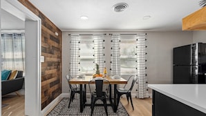 A modern kitchen with a wooden accent wall, a dining table with chairs, and a black refrigerator. - Clearwtr10min2beach&2min2 Dunedindwtn/king bed (Clearwater)