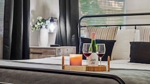 A bed with a bedside table holding a candle, two glasses of wine, and a bottle of jam jar. - Clearwtr10min2beach&2min2 Dunedindwtn/king bed (Clearwater)