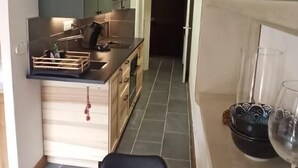A modern kitchen with grey cabinets, a wooden dining table, and a wine glass on the right. - Bright 30 M² With Balcony   Center Villa (Le Monêtier-les-Bains)