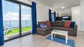 A modern living room with a sectional sofa, a glass coffee table, and a view of the sea through large sliding doors.