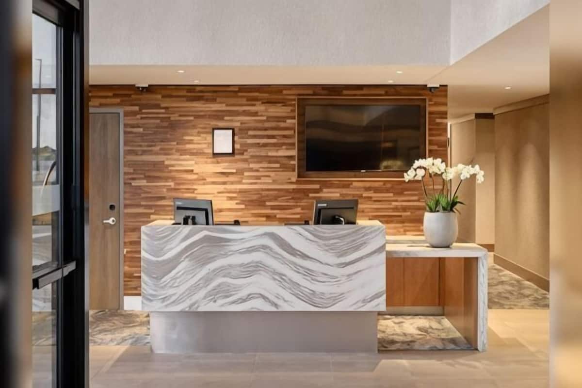 A reception desk with a marble top, a wooden wall panel, a mounted television, and a potted plant.