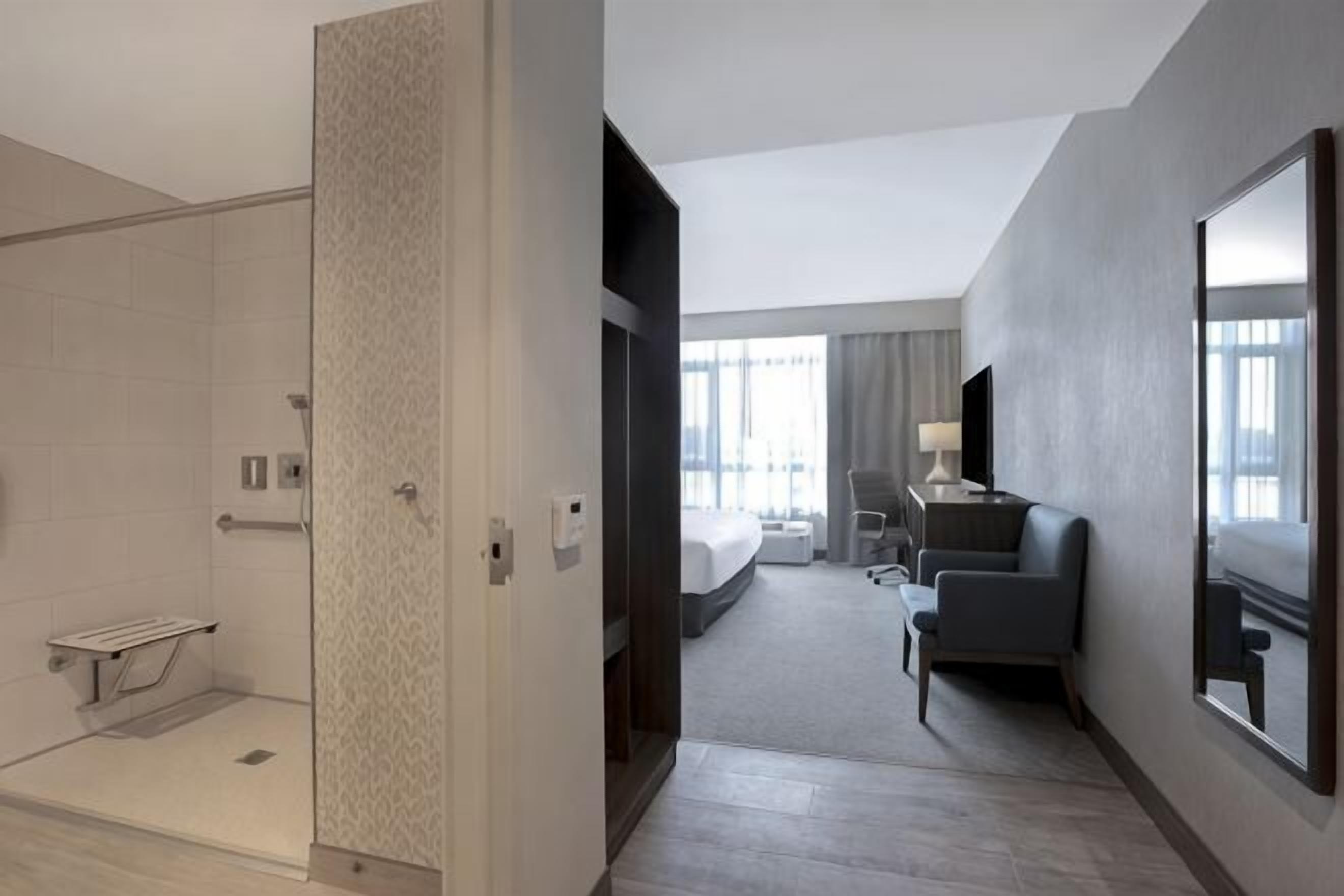 Una habitación de hotel con ducha, cama, escritorio, silla y un amplio ventanal.