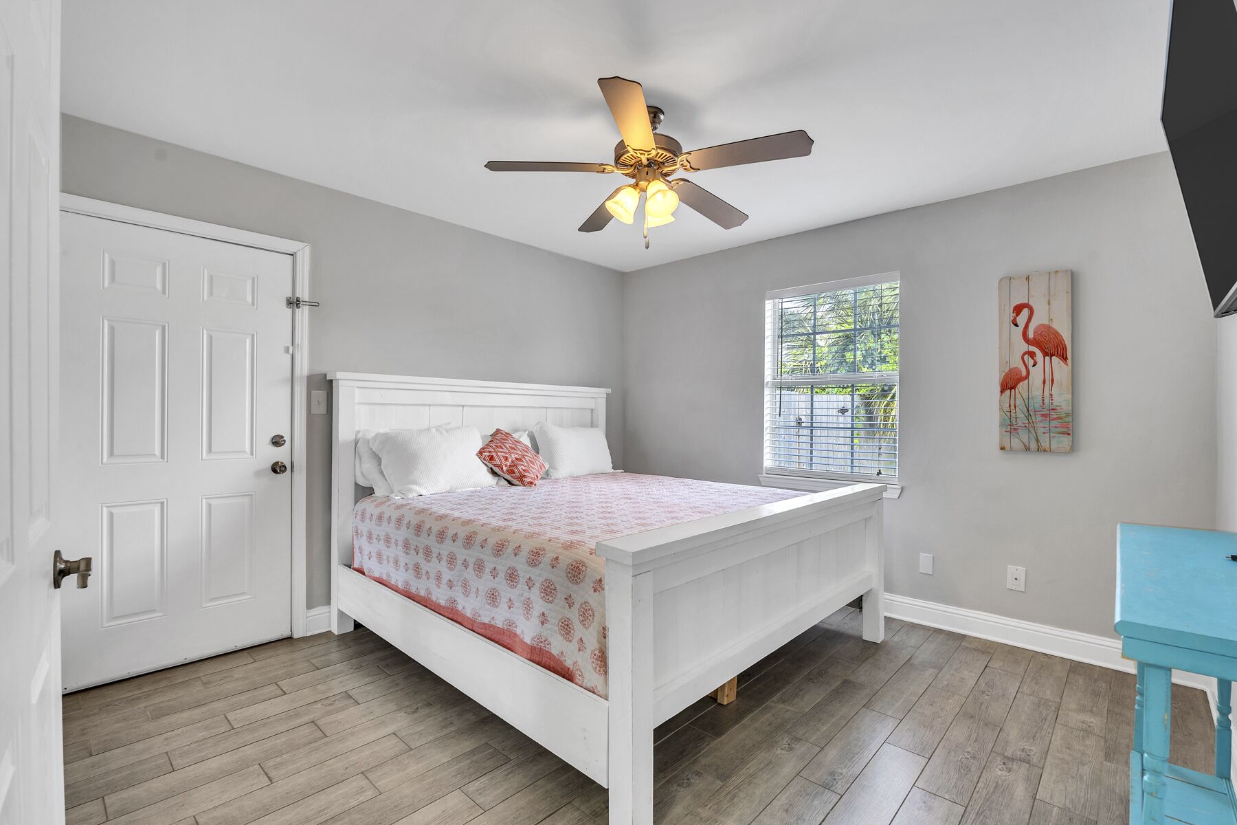 A bedroom with a white bed, a ceiling fan, a window with blinds, and a door.