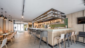 Zona de bar moderna con taburetes altos, una barra con estantes llenos de vasos y un televisor montado en la pared.