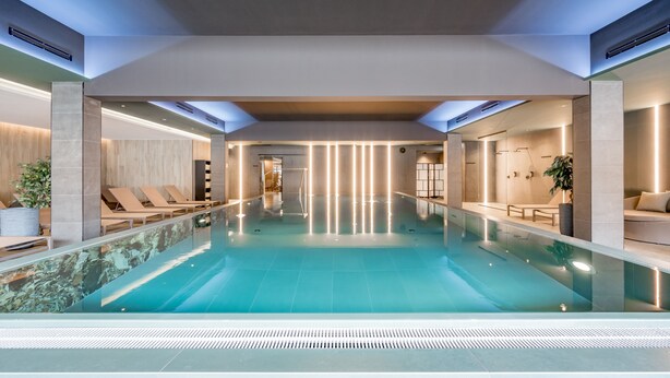 Piscina interior moderna con vista despejada del área de la piscina, sillas de descanso y un rincón de estar con una planta.